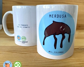 Pode incluir: Caneca de cerâmica branca com um círculo azul e uma criatura de desenho animado marrom com o texto "MERDUSA" e "@IL_CULOMBO". O outro lado da caneca tem o texto "SII PUNGENTE CON GLI STRON*II" e um logotipo com um pássaro e uma flecha.