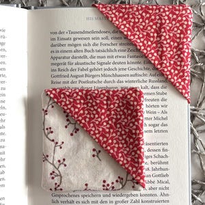 Puede incluir: Dos marcadores de tela hechos a mano. Uno es rojo con un estampado floral blanco, y el otro es blanco con un estampado floral rojo. Están colocados en las páginas de un libro abierto.