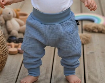 May include: A white short-sleeved bodysuit paired with dusty blue muslin pants featuring a wide, elasticized waistband and matching ribbed cuffs at the ankles. The pants have a textured, crinkled fabric finish and a relaxed, loose-fitting silhouette.
