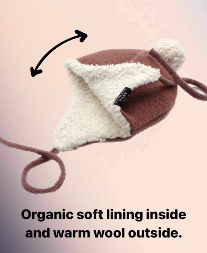 Peut inclure: Un bonnet en laine marron avec un pompon blanc, des oreillettes et de longs liens. L'int&eacute;rieur pr&eacute;sente une doublure en polaire blanche. Une &eacute;tiquette noire avec le texte ANNA KARINNA est visible. Le texte Organic soft lining inside and warm wool outside est pr&eacute;sent.