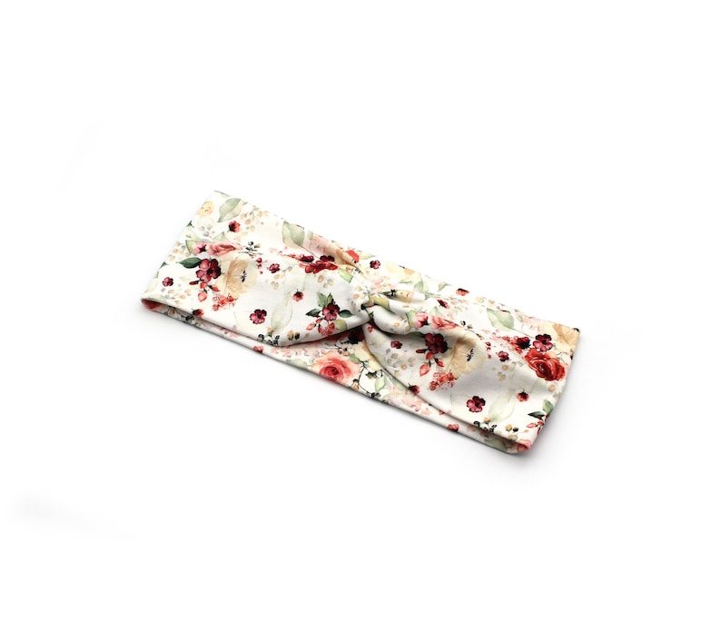 May include: A floral headband featuring a cream background with a pattern of red, pink, and green flowers and leaves. The headband is knotted at the top, creating a stylish accessory.