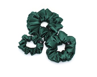 May include: Three dark green satin scrunchies of varying sizes are arranged on a white background. Each scrunchie has a label with white text. The fabric has a slight sheen, and the scrunchies appear soft and voluminous. These hair accessories are a stylish addition to any hairstyle.