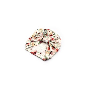 May include: A floral print baby turban in cream, red, and yellow. The turban features a knotted design and is made of soft fabric. The pattern includes roses and other flowers.