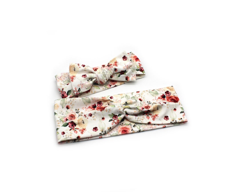 May include: Two floral headbands with a white background. One headband is a knotted style, and the other is a bow. The headbands feature a pattern of red, pink, and yellow roses with green leaves. The headbands are made of soft fabric.