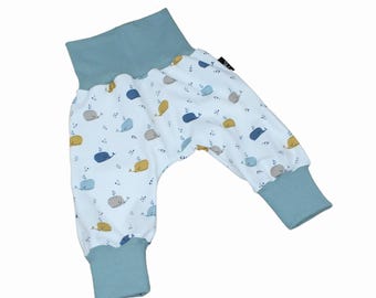 Puede incluir: Pantalones de bebé con fondo blanco y estampado de ballenas azules, amarillas y grises. Los pantalones tienen cintura y puños azul claro. La tela es suave y cómoda.