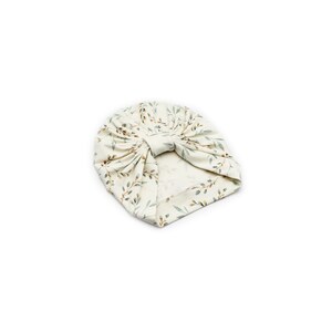 May include: A cream-colored baby turban with a botanical print of green and brown leaves and stems. The turban is knotted at the top and is made of soft fabric. The head covering is designed for infants.