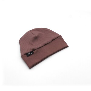 Może przedstawiać: Fioletowo-szara czapka beanie z prążkowanej dzianiny z wywiniętym brzegiem. Czapka ma małą czarną metkę z białym napisem w pobliżu brzegu. Czapka jest wykonana z miękkiego, elastycznego materiału.