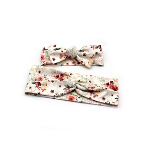 May include: Two floral headbands. The larger headband is a wide band with a twist detail. The smaller headband is a bow. Both are white with a pattern of red, pink, and yellow roses with green leaves.