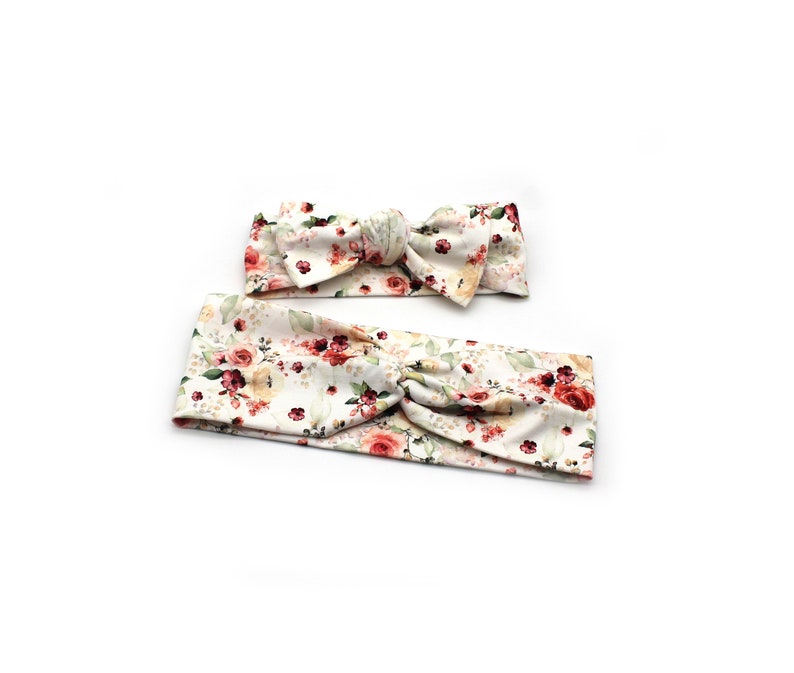 May include: Two floral headbands. The larger headband is a wide band with a twist detail. The smaller headband is a bow. Both are white with a pattern of red, pink, and yellow roses with green leaves.