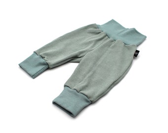 May include: A pair of baby pants in a soft, ribbed fabric. The pants are a muted green color with contrasting teal cuffs and waistband. The fabric appears to be a comfortable, stretchy material, suitable for infants.