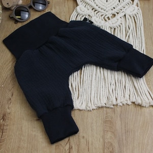 May include: Dark navy blue baby pants with ribbed texture and elastic cuffs. The pants are folded, showcasing the soft fabric and design. The garment is likely for infants or toddlers.