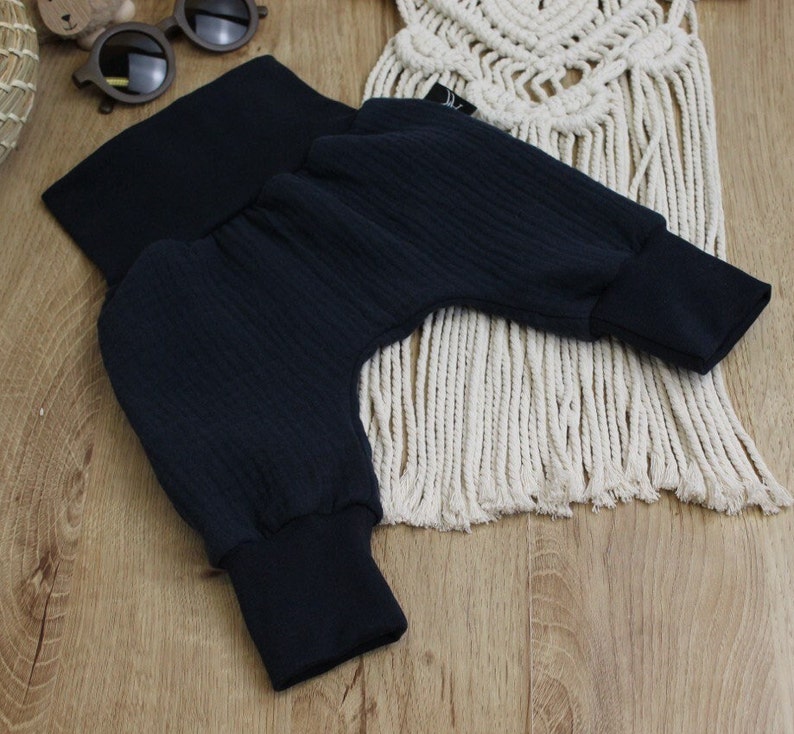 May include: Dark navy blue baby pants with ribbed texture and elastic cuffs. The pants are folded, showcasing the soft fabric and design. The garment is likely for infants or toddlers.