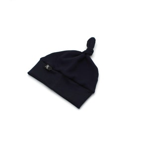 May include: A navy blue baby knot hat with a small, round, black logo on the folded brim. The hat is made of soft material and has a knotted top. The hat is designed for infants.