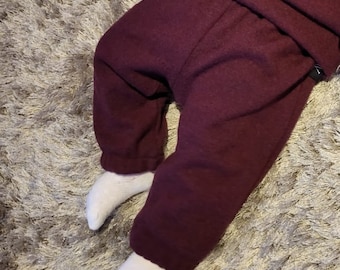 May include: A pair of burgundy sweatpants with a matching top. The pants have a relaxed fit with elastic cuffs at the ankles. The outfit is made of a soft, textured fabric. White socks are visible.