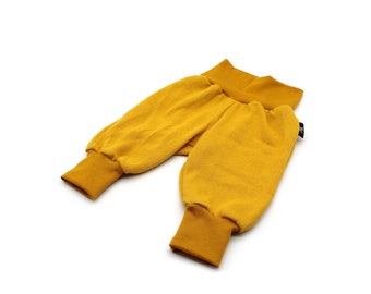 May include: Mustard yellow baby pants with ribbed cuffs and a matching waistband. The pants are made of a soft, textured fabric and are designed for comfort. The garment is displayed on a white background.