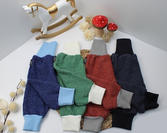 May include: A collection of colorful baby pants in shades of blue, green, red, and black. Each pair features a contrasting cuff and waistband. The pants are arranged on a white surface, with decorative elements in the background.