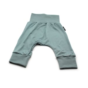 May include: Light teal baby trousers with a high waistband and cuffed ankles. The trousers are made of a soft, stretchy fabric, designed for comfort and movement. The design features a relaxed fit, suitable for everyday wear.