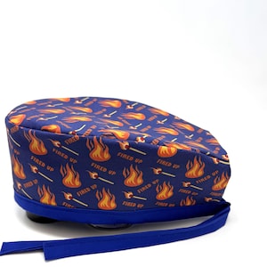 May include: A blue surgical scrub hat with a pattern of orange flames and the text "Fired Up" repeated throughout.