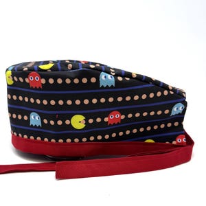 May include: A black scrub hat with a red tie. The hat has a pattern of Pac-Man ghosts and dots on a black background.