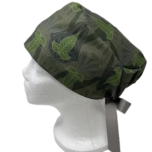 May include: A green and gray patterned scrub cap with a leaf design. The cap is tied in the back with a gray ribbon. The cap is displayed on a white mannequin head.