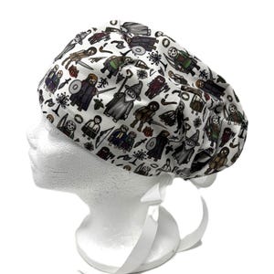 May include: White scrub cap with a repeating pattern of cartoon characters in brown, grey, and green. The cap has a white ribbon tie at the back. The cap is on a white mannequin head. The characters are in various poses.