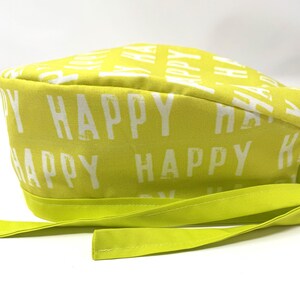 May include: A lime green scrub cap with the word "HAPPY" printed in white. The cap has a long, matching tie. The fabric is a bright, solid lime green with the word "HAPPY" repeated across the surface.