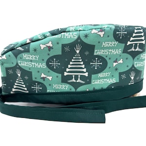 May include: A teal scrub cap with a festive Christmas pattern. The cap features white bone-shaped accents, Christmas trees, and the words "MERRY CHRISTMAS." A dark green band and ties complete the design.