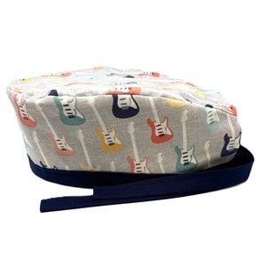 Op de afbeelding: Een grijze scrubmuts met een blauwe rand en een patroon van kleurrijke elektrische gitaren.