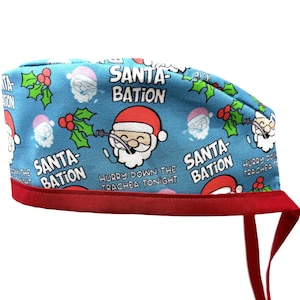Könnte beinhalten: Eine blaue und rote OP-Mütze mit Weihnachtsmotiv. Sie zeigt ein sich wiederholendes Muster von Weihnachtsmann mit dem Text "Santa-Bation" und "Hurry down the trachea tonight".