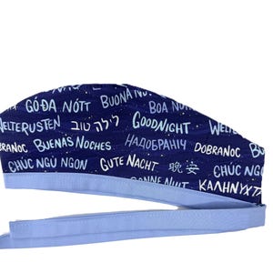 May include: A navy blue scrub cap with the words "Goodnight" in multiple languages. The cap has a light blue band and ties. The text includes phrases like "Buona Notte" and "Buenas Noches".