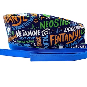 Może przedstawiać: Niebieski czepek chirurgiczny z nadrukowanymi na nim różnymi terminami medycznymi w różnych kolorach, w tym "Fentanyl", "Ketamina", "Lidocaina" i "Neostigmina".