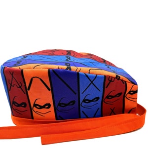 Może przedstawiać: Kolorowy czepek chirurgiczny z wzorem Teenage Mutant Ninja Turtles. Czepek ma pomarańczową tasiemkę.