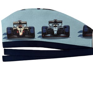 May include: A light blue scrub cap featuring a repeating pattern of Formula 1 race cars in red, white, and black. The cap has a dark blue band and ties. The design is a cartoon style.