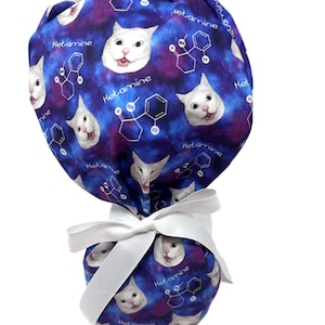 May include: A blue and purple patterned scrub cap featuring white cat faces and the word "Ketamine" with a chemical structure. The cap is tied with a white ribbon.