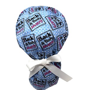 May include: A blue patterned scrub cap with the text "Back & Body Hurts" in white and pink. The cap is tied with a white bow. The background is white.
