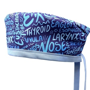 Może przedstawiać: Niebieski i jasnoniebieski czepek chirurgiczny z wzorem anatomicznych terminów napisanych w stylu graffiti. Czepek ma jasnoniebieski sznurek.