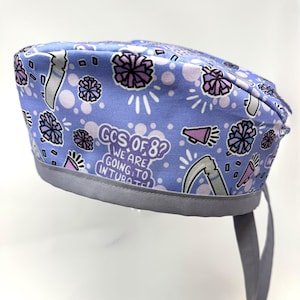 Op de afbeelding: Een lichtblauwe chirurgische scrub-muts met een grijze rand en banden. De muts heeft een print van pompoenen, megafoons en de tekst "GCS of 8? We are going to intubate".