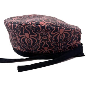 May include: A black and coral patterned scrub cap featuring an octopus design. The cap has a black band and ties. The fabric has a repeating pattern of octopuses and decorative swirls. This cap is designed for medical professionals.