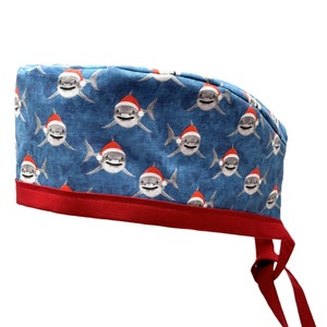 May include: A blue scrub hat with a red trim and a pattern of white sharks wearing Santa hats.