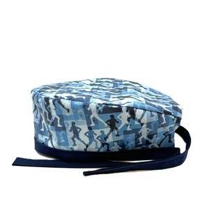 May include: Blue and gray patterned surgical scrub hat with a navy blue tie. The pattern features silhouettes of people running.