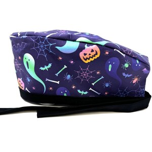 May include: A purple scrub hat with a Halloween theme. The hat features a pattern of ghosts, pumpkins, bats, spiderwebs, and bones in a rainbow color scheme.
