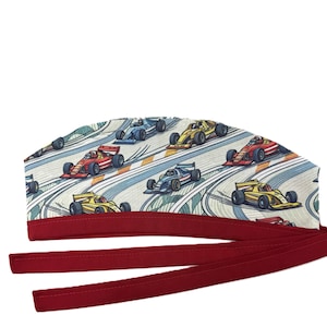 Może przedstawiać: Czapka chirurgiczna z powtarzającym się wzorem kolorowych samochodów wyścigowych na torze. Czapka ma czerwony pasek i długie czerwone wiązania do mocowania. Samochody wyścigowe są w kolorach czerwonym, żółtym, niebieskim i białym.