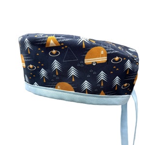 May include: A blue scrub hat with a white and yellow pattern of trees, a tent, and a camper. The hat has a light blue ribbon and ties.