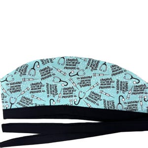 May include: A light blue scrub cap featuring a repeating pattern of black stethoscopes, syringes, and the text "Laughter isn't the best medicine... Propofol is." The cap has a solid black fabric band at the bottom and two long black fabric ties.