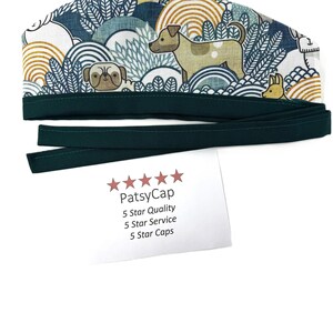 May include: A patterned surgical cap with a dark green band and ties. The cap features a repeating design of dogs, trees, and abstract shapes in shades of blue, white, and gold. The text "PatsyCap" is visible on a white card.