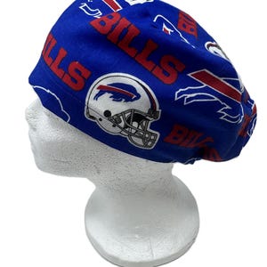 May include: A blue scrub cap featuring a repeating pattern of the Buffalo Bills football team logo, including white helmets with red and blue stripes, and the word BILLS printed in red block letters across the fabric surface.