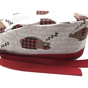 Op de afbeelding: Een grijze en witte scrubmuts met een rode rand en een herhalend patroon van beren die pyjama's dragen en de tekst "Maak de beer niet wakker".