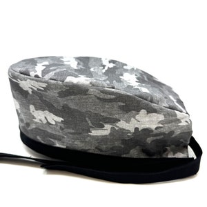 Op de afbeelding: Een grijze en witte camouflage scrub-muts met een zwart elastiek.