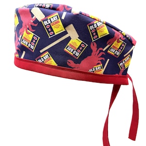 May include: A blue and red surgical scrub hat with a pattern of Old Bay seasoning cans, crabs, and wooden mallets. The hat has red ties.