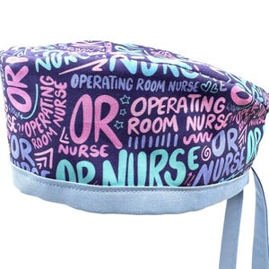May include: A purple scrub hat with a blue trim and ties. The hat has a repeating pattern of the words "OR", "Operating Room", and "Nurse" in pink, blue, and white.